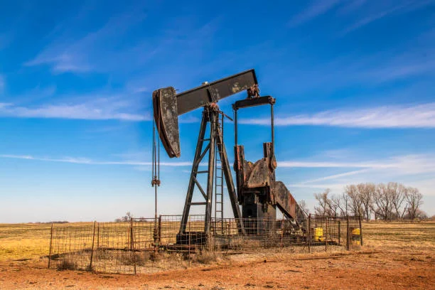 An image of a solitary, weathered oil pumpjack in a dry, barren field under a clear sky, surrounded by a metal fence. It serves as a reminder of the industry’s legacy, highlighting concerns about greenhouse gas emissions and the importance of managing abandoned and orphan oil and gas wells.