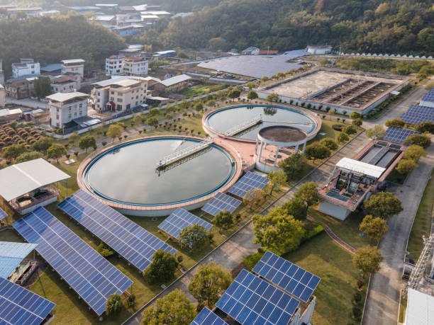 Aerial shot of a sustainable water treatment facility with circular settling tanks and adjacent solar panel arrays, showcasing integration of renewable energy solutions in industrial operations to reduce carbon footprint and promote green energy use.